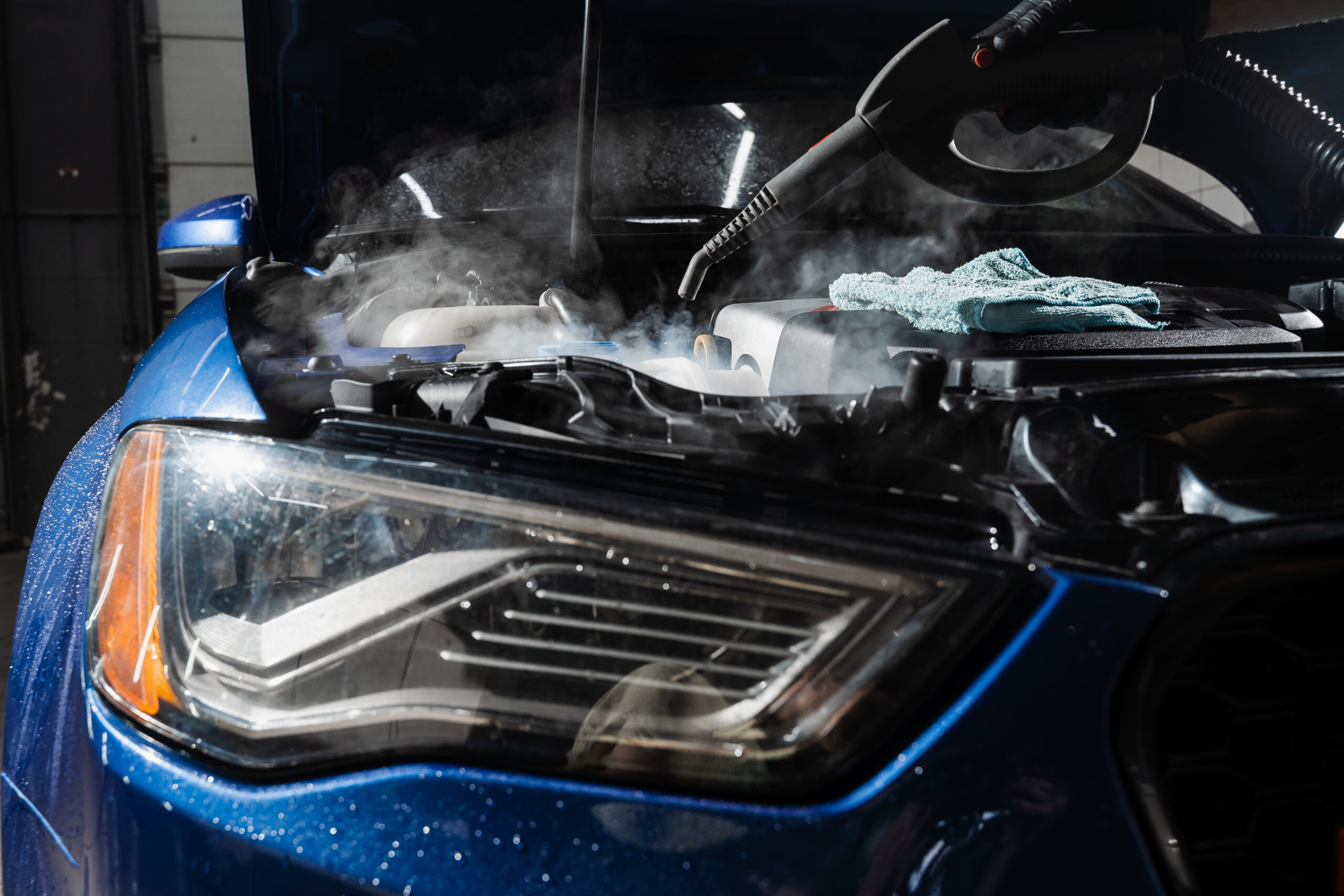 Steam washing a car engine to remove dust and dirt during a professional detailing service